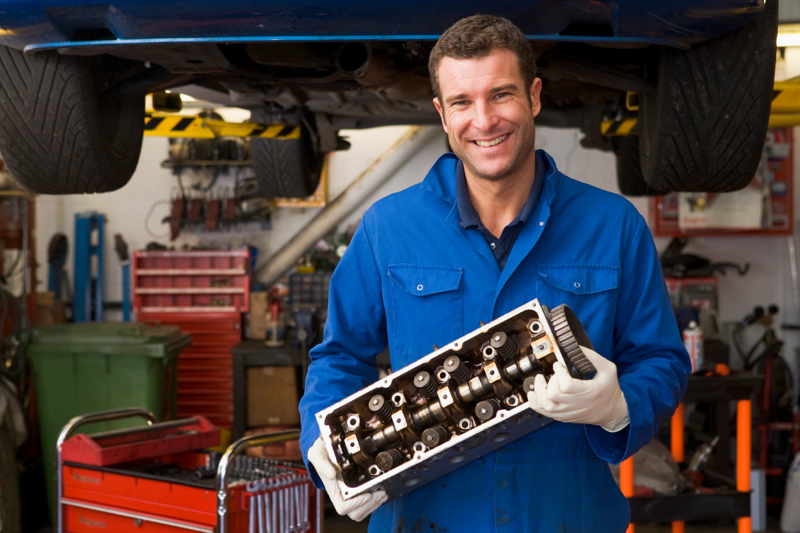 Mechaniker mit Motorbauteil unter der Hebebühne